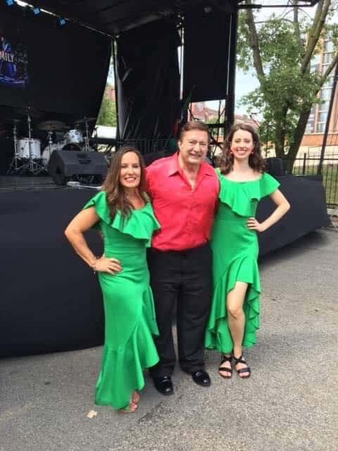 Joe Martino with two Volare Dancers in green dresses beside an outdoor stage