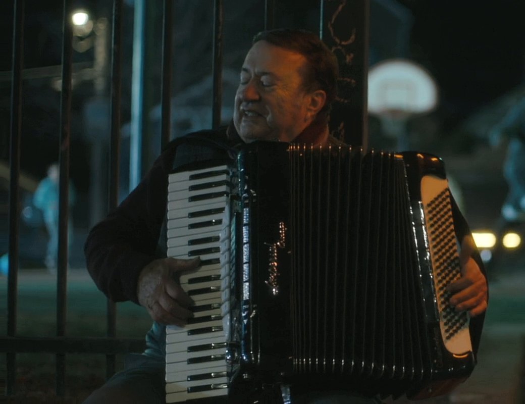 Joe Martino playing accordion and singing at night in a Chicago park, a still from the film Alex/October
